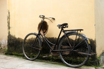 Fototapeta na wymiar my grandpa's lifestyle - raised old black bycicle against a yellow mossy wall with rice field worker hat