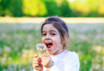  Beautiful little girl  laughing with dandelion flower in sunny spring park. Happy cute kid having fun outdoors at sunset.