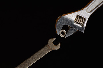 One adjustable wrench, gives one a spanner nut isolated on a black background