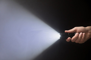 Black flashlight with a beam of light in male's hand isolated from right side of the frame on black background copyspace - obrazy, fototapety, plakaty