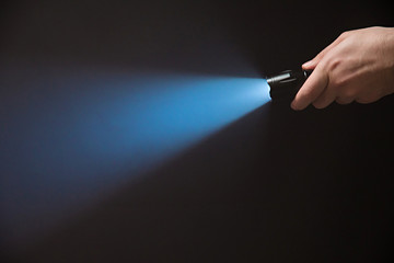 Male hand holding a led flashlight with a narrow blue beam on a black background, leaving the right...