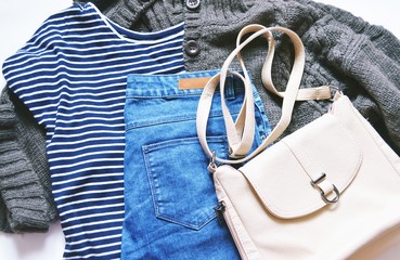 Flat lay fashion women's clothes photo/ Autumn and winter fashion blogger's outfit. Striped tshirt, brown wool knitted cardigan, blue jeans from denim and beige bag. Casual style, trendy wear