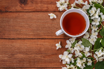 Cup of black tea and white Jasmine flowers on a brown wooden background