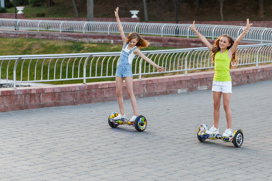 Happy girls riding on hover boards or gyroscooters outdoors at sunset in summer. Active life concept