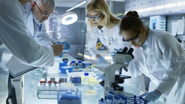 Team of Medical Research Scientists Work on a New Generation Disease Cure. They use Microscope, Test Tubes, Data Implementing Technology. Laboratory Looks Busy, Bright and Modern. 
