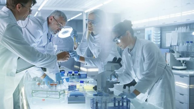Team of Medical Research Scientists Work on a New Generation Disease Cure. They use Microscope, Test Tubes, Micropipette and Writing Down Analysis Results. Laboratory Looks Busy, Bright and Modern. 