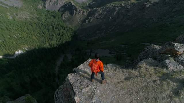 Hiker with backpack standing on top of a mountain with raised hands and enjoying sunrise aerial slow motion 4k