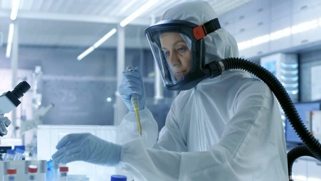 Medical Virology Research Scientist Works in a Hazmat Suit with Mask, She Takes out Test Tubes from Refrigerator Box. She Works in a Sterile High Tech Laboratory/ Research Facility. 4K UHD.