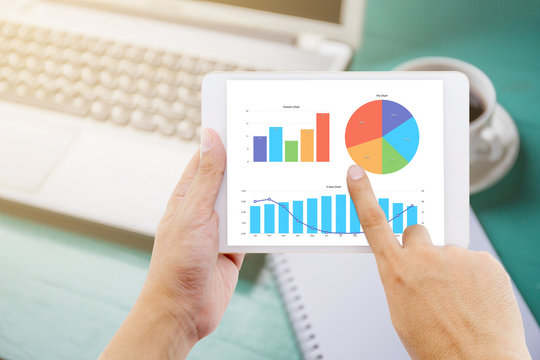 The lablet in your hand with graph on the table and laptop