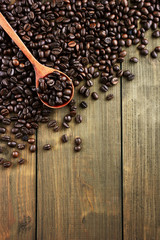 Coffee beans on spoon and wooden background.