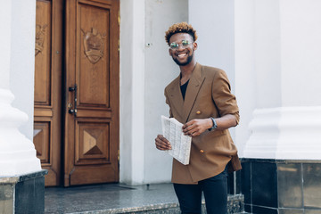 Portrait of an African American man in a jacket  with a newspaper and smarphone on the background of office buildings