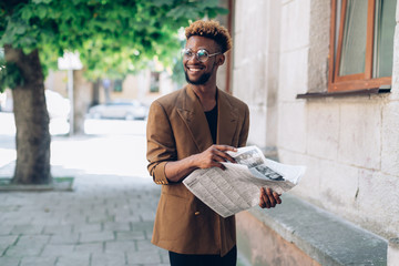 Portrait of an African American man in a jacket  with a newspaper and smarphone on the background of office buildings