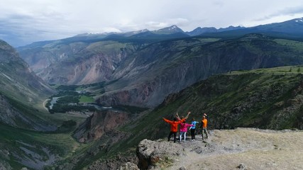 Group of friends are happy that climbed to the top the mountain. They hug and jump. Looking into the distance with back the camera. aerial slow motion 4k,