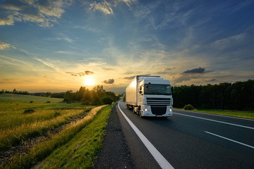 White truck driving on the asphalt road in rural landscape at sunset - obrazy, fototapety, plakaty