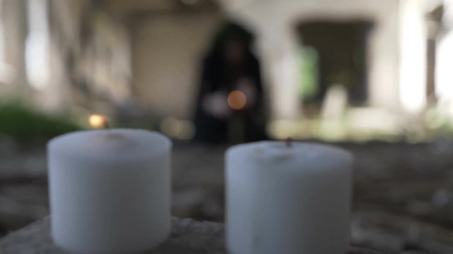 Macabre young witch cursing and putting spells in a ceremony with candles in a ruined castle