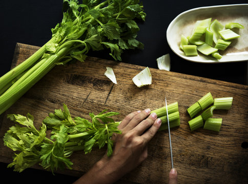 Aerial view of hands with knife cutting celery on wooden cut board
