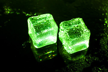 Green ice cubes on black wet table.
