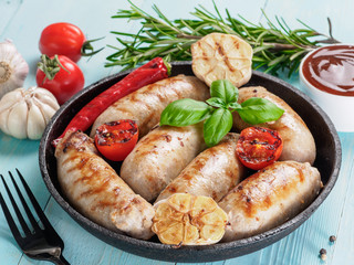 Chicken homemade sausages, sauces ketchup and vegetables and herbs on blue wooden background. Grilled sausages and grilled vegetables in black iron pan