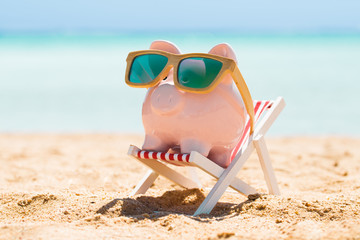 Piggy Bank With Wooden Sunglasses On The Deck Chair - obrazy, fototapety, plakaty