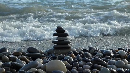 Zen stones on the beach breaking by sea surf. Pebble tower destroying by strong water wave with lot of foam and splashes.Tranquility and disturbance concept. - Powered by Adobe