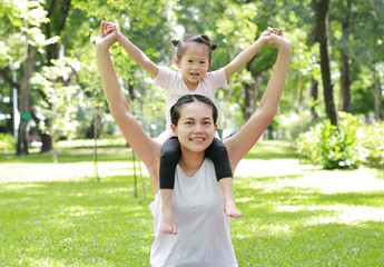 Obraz premium Child girl play riding on mother neck in park.