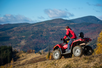 Male on an ATV riding down the hilly road on a background of mountains, forest and blue sky. The concept of an active holiday in the mountains