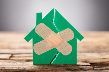 Closeup Of Broken House With Crossed Band Aid