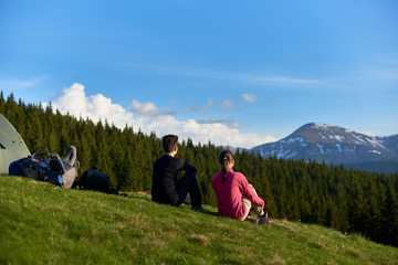 Fototapeta premium Rearview shot of two women sitting on top of a hill near their tent enjoying beautiful mountains view copyspace lifestyle activity sport health friendship travelling