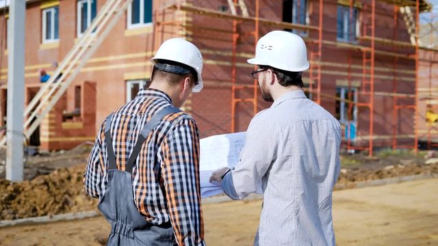 A man the foreman and the bearded customer are discussing the plan for the construction of a new country house in a cottage settlement