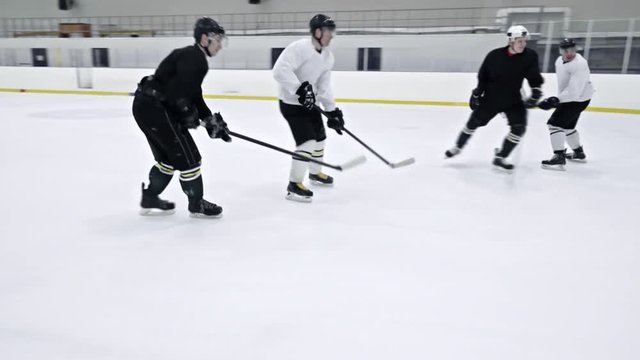Tracking of ice hockey player in white uniform dribbling puck and doing reverse pass to teammates during practice in rink