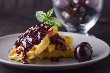 Waffles with homemade cherry jam and mint leaves, glass cup of cherries in background