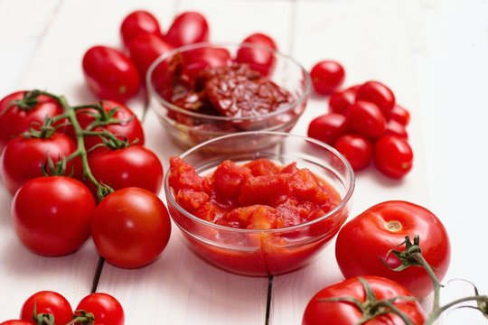 Several common types of tomatoes on white wooden table. Cherry, regular,canned peeled,sun dried in olive oil.