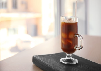 Glass cup of cold brew coffee and straw on light blurred background