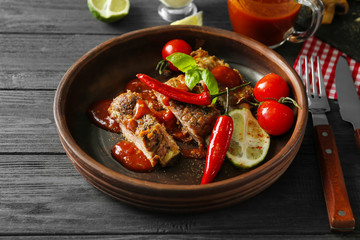 Delicious grilled spare ribs with vegetables and sauce in bowl on wooden table