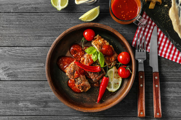 Delicious grilled spare ribs with vegetables and sauce in bowl on wooden table