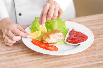 Female hands adding lemon slice to yummy fried chicken thigh with sauce on white plate