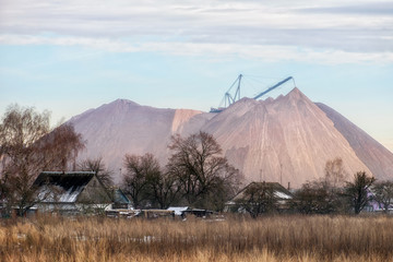 Extracting and mining potassium and magnesium salts.Large excavator machine and Huge mountains of waste ore in the extraction of potassium on the background of the houses of local residents. 