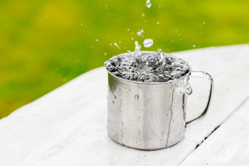 A steel mug with water and sprays on a white wooden table on nature background, life concept