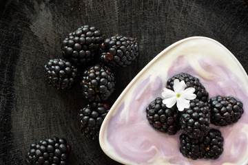 Blackberries with yogurt on black wooden background. Refreshing breakfast