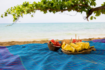 Beautiful set of prepared fruits on vivid blue cloth at the beach side with tree branch in the background