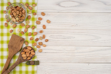 Beans in a glass bowl and a wooden spoon on a white table.