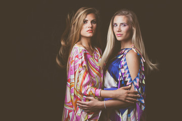 two blonde young women beauty fashion portrait in colorful silky dress