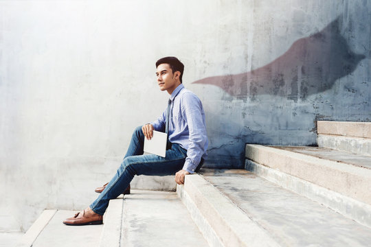 Power, Success and Leadership in Business concept, Young man sitting on office Outdoor Stair and looking forward with superhero blanket shadow shade on the wall, Side view