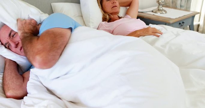 Senior man lying on bed and covering his ears with pillow