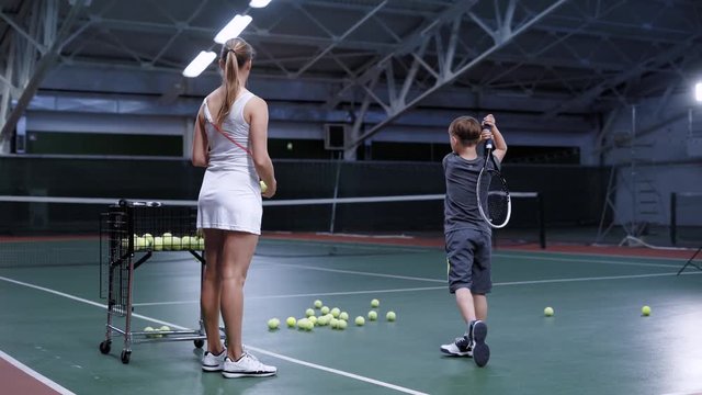 Woman throwing ball while practicing hit with little boy on tennis court