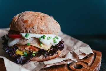 A real burger on a wooden background. With a large and juicy cutlet tender cheese sauce and mustard. Rustic