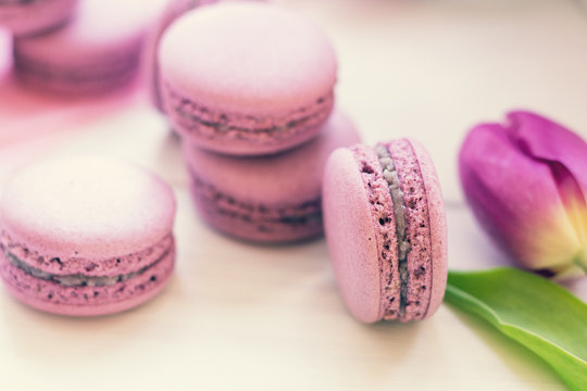 Violet sweet delicious macaroons and fresh tulips on white background. Cup of hot tea. Shallow depth of field. Coloring toned photo.