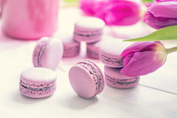 Obraz na płótnie Canvas Violet sweet delicious macaroons and fresh tulips on white background. Cup of hot tea. Shallow depth of field. Coloring toned photo.