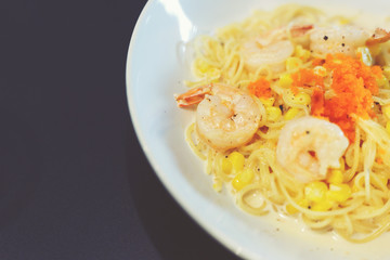 Carbonara spaghetti cream with shrimp in white dish put on black table.