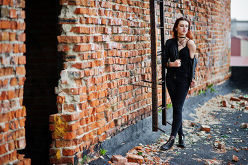 Red haired punk girl wear on black at the roof against brick wall with iron ladder.